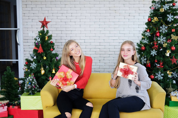 Усміхаючіся дівчата з кавказу тримають велику коробку з подарунками на дивані у вітальні. вони так радіють з християнства і святкують новорічну вечірку. Життя лесбіянок у святковій концепції - Фото, зображення