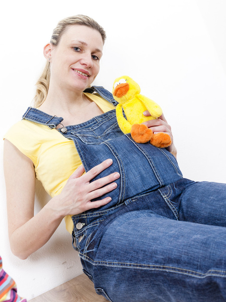赤ちゃんのおもちゃを持って座っている妊娠中の女性の肖像画 - 写真・画像