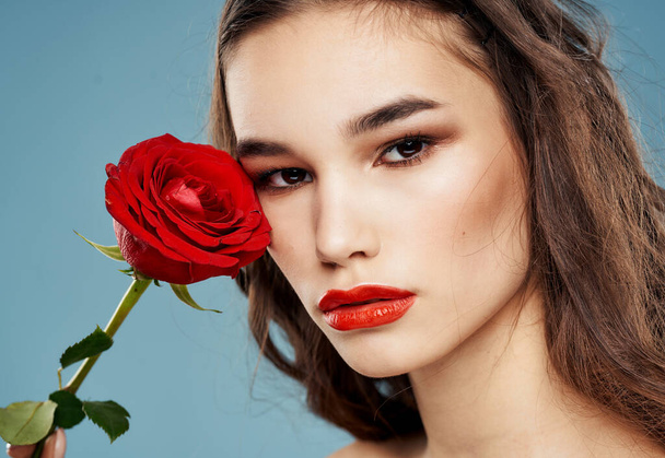 A woman holds in her hand a red flower on a blue background and makeup on her face - Fotografie, Obrázek