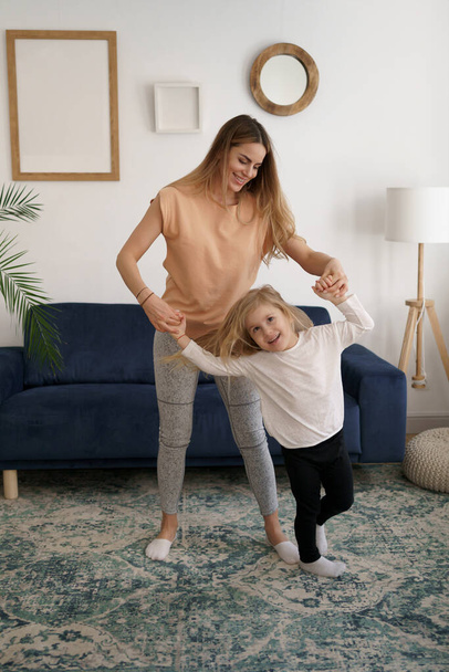 Happy fit sporty mother and funny active daughter having fun dancing together at home - Photo, Image