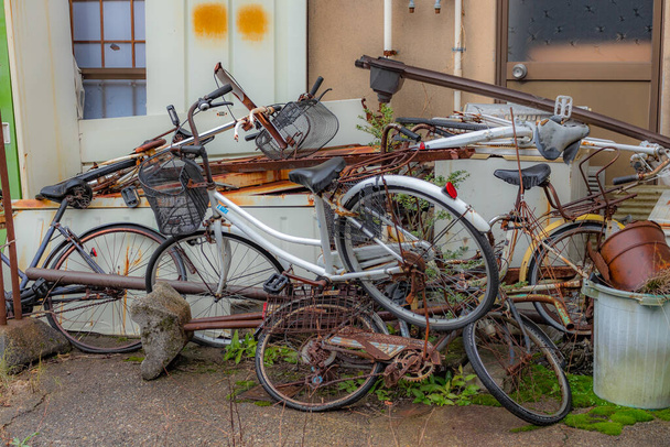 Kolekcja starych wyrzuconych rowerów i metalu, przed opuszczonym japońskim domem, Kanazawa, prefektura Ishikawa, Japonia. - Zdjęcie, obraz