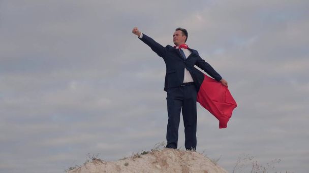 Superbohater w czerwonym płaszczu przeciwko błękitnemu niebu, biznesmen w garniturze, szybki sukces w biznesie, dyrektor prowadzący główne statystyki przedsiębiorstwa, menedżer dokonujący nowych odkryć - Zdjęcie, obraz