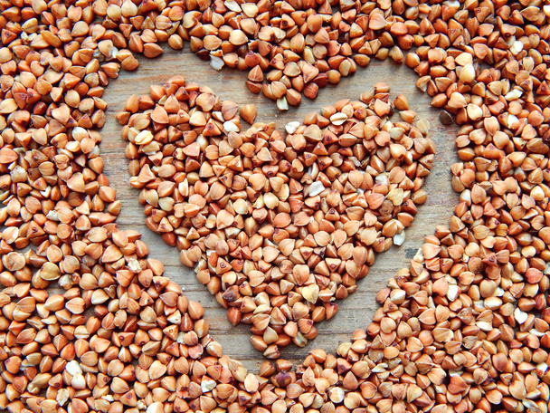 Buckwheat grains in a shape of heart on wooden table - Photo, Image