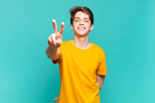 young boy smiling and looking happy, carefree and positive, gesturing victory or peace with one hand - Foto, Imagen