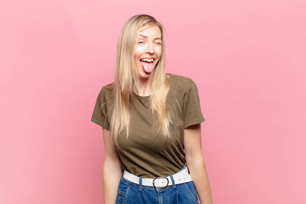 young blond pretty woman with cheerful, carefree, rebellious attitude, joking and sticking tongue out, having fun - Foto, Imagem
