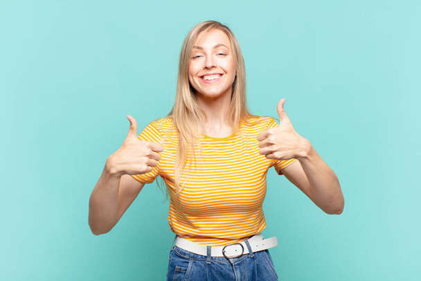 young blond pretty woman smiling broadly looking happy, positive, confident and successful, with both thumbs up - Foto, imagen