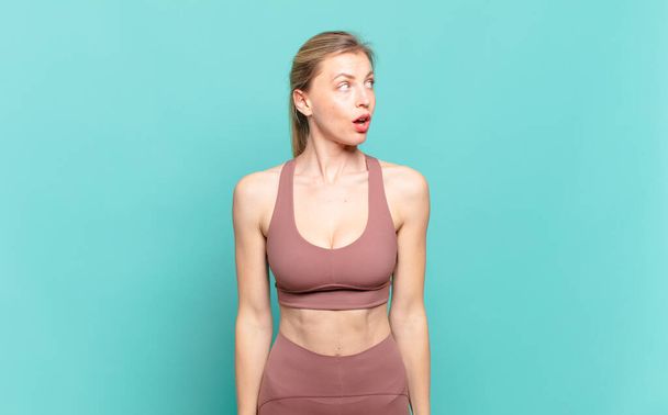 young blond woman feeling shocked, happy, amazed and surprised, looking to the side with open mouth. sport concept - 写真・画像