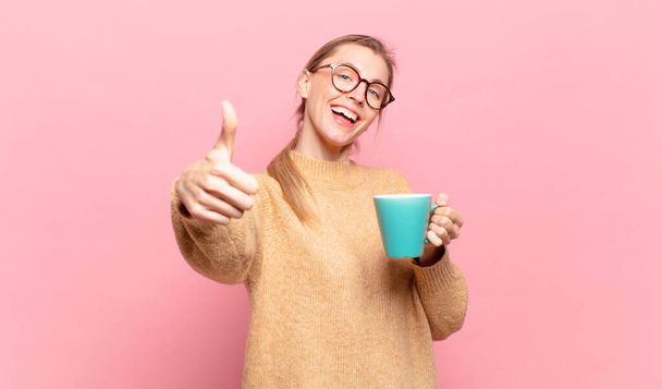young blond woman feeling proud, carefree, confident and happy, smiling positively with thumbs up. coffee concept - Foto, imagen