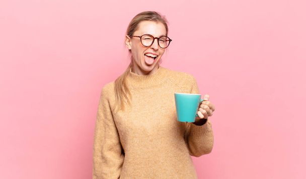 young blond woman with cheerful, carefree, rebellious attitude, joking and sticking tongue out, having fun. coffee concept - Foto, imagen