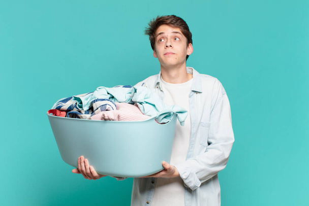 young boy shrugging, feeling confused and uncertain, doubting with arms crossed and puzzled look washing clothes concept - Foto, Imagem