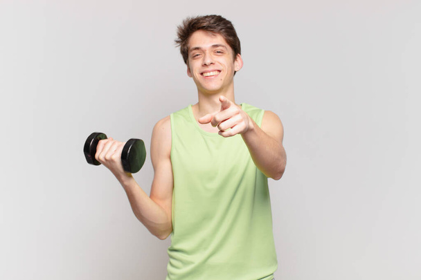 young boy pointing at camera with a satisfied, confident, friendly smile, choosing you. dumbbell concept - Foto, afbeelding
