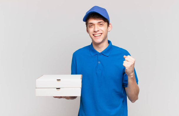 young pizza deliver boy feeling shocked, excited and happy, laughing and celebrating success, saying wow! - Fotoğraf, Görsel