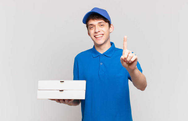 young pizza deliver boy smiling proudly and confidently making number one pose triumphantly, feeling like a leader - Foto, immagini