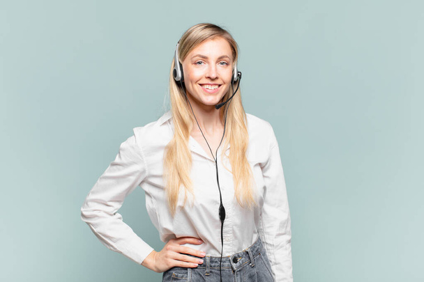 young blond telemarketer woman smiling happily with a hand on hip and confident, positive, proud and friendly attitude - Foto, immagini