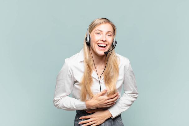 young blond telemarketer woman laughing out loud at some hilarious joke, feeling happy and cheerful, having fun - Foto, imagen