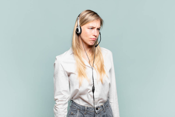 young blond telemarketer woman feeling sad, upset or angry and looking to the side with a negative attitude, frowning in disagreement - Fotografie, Obrázek