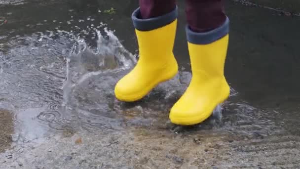 黄色のゴムブーツの水たまりをジャンプします。雨の中を歩くと、悪天候が子供の頃に落ち、湿った水たまりを通って実行してお楽しみください。顔のない足のビデオ. - 映像、動画