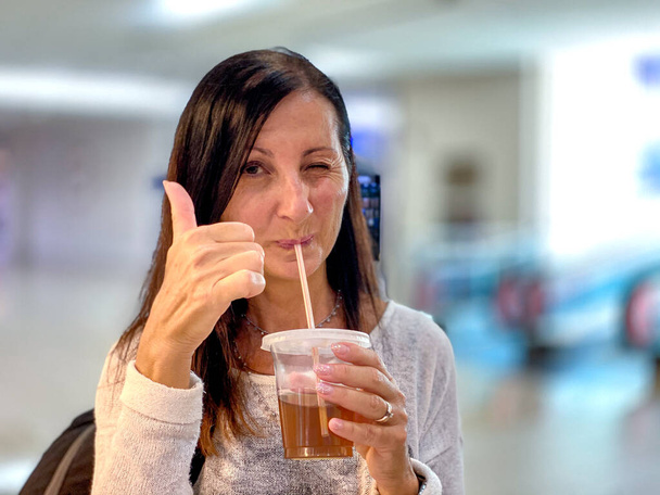 Glückliche Frau schlürft erfrischendes Getränk mit erhobenem Daumen. - Foto, Bild