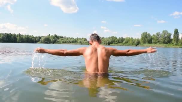 Egy fiatal férfi meztelenül merül a vízbe egy tó közelében az erdőben a természetben. Úszás és pihenés - Felvétel, videó