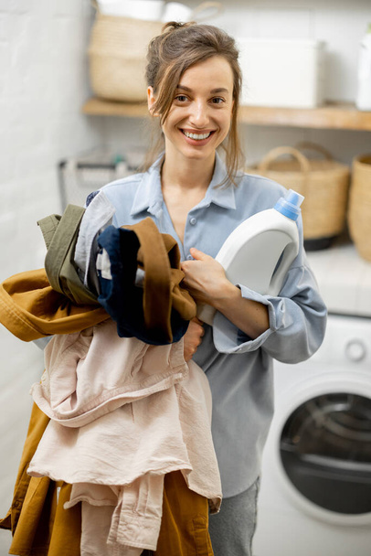 Жінка з чистим одягом і миючим засобом в пральні вдома
 - Фото, зображення