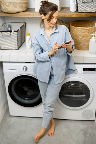 Woman with phone in the laundry room - Photo, Image