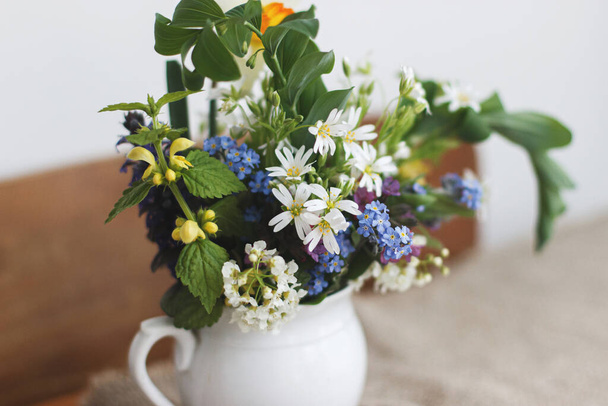 Beautiful spring wildflowers in vintage cup on rustic wooden table. Blooming colorful flowers of ajuga, forget-me-nots, daffodils, pulmonaria, rabelera holostea closeup. Countryside meadow bouquet - Photo, Image