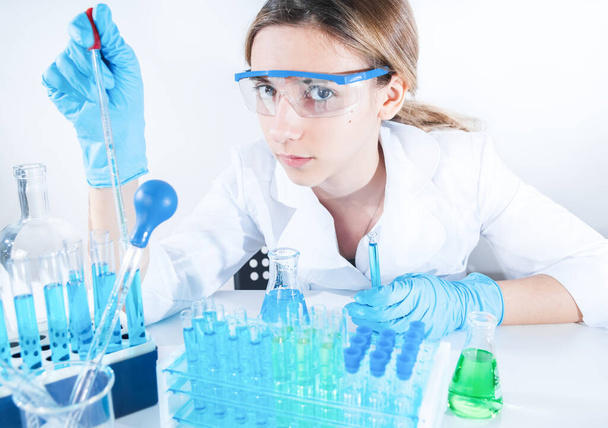 Koruyucu gözlüklü ve maskeli profesyonel kadın bilim adamı laboratuvarda reaktörlerle deney yapıyor. Reçeteli ilaç üretimi. Coronavirus salgını durması. Tıp konsepti - Fotoğraf, Görsel