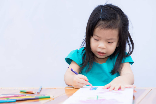 Meisje doet kunst op kleurboek met houtkleuren. Kind genieten van het maken van ambachten. Oefen creativiteit bij kinderen. Studeer thuis. 3-4 jaar oude kinderen dragen groene kleren. Geïsoleerde witte wand achtergrond. - Foto, afbeelding