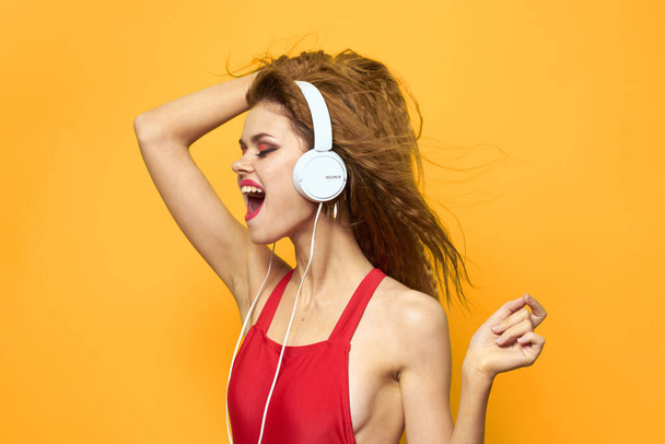 音楽を聴くヘッドフォンの女性赤いTシャツの感情ファッション黄色の背景ライフスタイル - 写真・画像