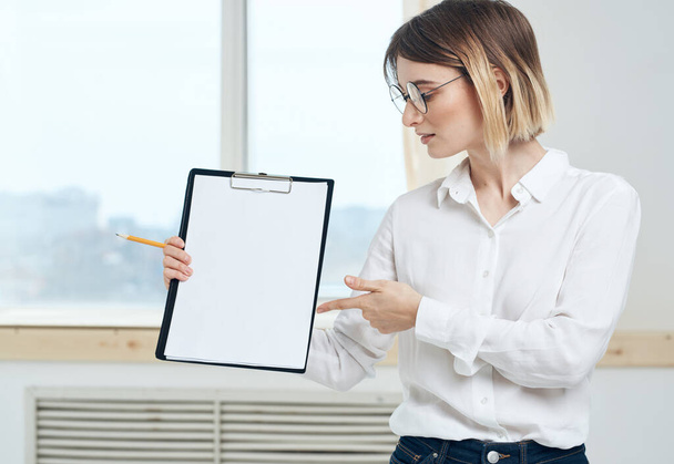 Una donna tiene una cartella con un foglio bianco di carta e una finestra sullo sfondo - Foto, immagini