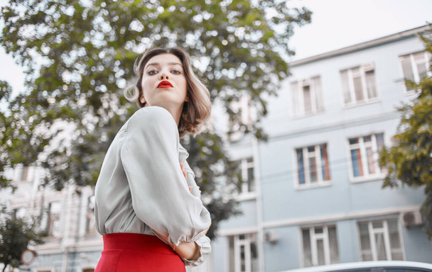 woman with red lips in a fashionable shirt near the building and green trees spring nature - Photo, Image