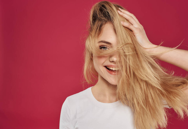 Onnellinen blondi koskettaa hiuksia kädet punaisella taustalla hauskoja tunteita rajattu näkymä - Valokuva, kuva