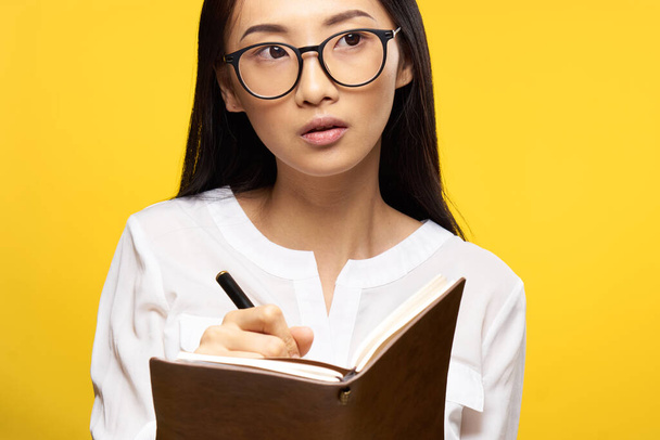 ノートパッド付きメガネのエレガントな女性手で教える学生黄色の背景 - 写真・画像