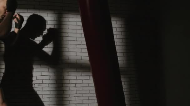 Стрельба человека с боксерской грушей возле кирпичной стены - Кадры, видео