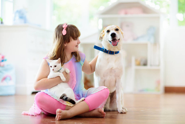 Το παιδί παίζει με τη γάτα και το σκύλο. Τα παιδιά παίζουν με το κουτάβι και το γατάκι. Κοριτσάκι και μεγάλος σκύλος στο σπίτι. Παιδιά και φιλία. Το παιδί κάθεται στο πάτωμα με το κατοικίδιο του. Φροντίδα των ζώων - Φωτογραφία, εικόνα