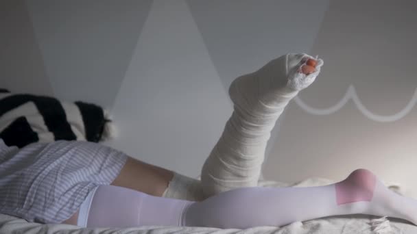Een vrouw met een gebroken been in gips en een samengestelde kous ligt 's morgens op het bed van het huis. - Video