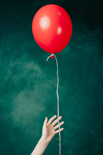 globo rojo inflable en una mano femenina sobre un fondo verde de cerca - Foto, Imagen