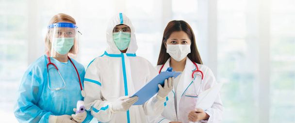 International doctor team. Hospital medical staff in hazmat suit, face shield and mask. Mixed race Asian and Caucasian doctor and nurse meeting. Clinic personnel with stethoscope. Coronavirus outbreak - Fotografie, Obrázek