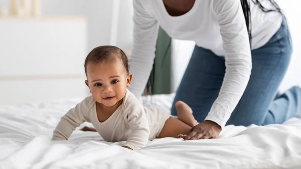 Aranyos kis afro-amerikai baba mászik az ágyban anyuval - Fotó, kép