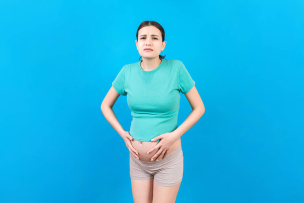 μια έγκυος κοπέλα που έχει στομαχόπονο στέκεται σε ένα έγχρωμο φόντο. απομονωμένα. - Φωτογραφία, εικόνα