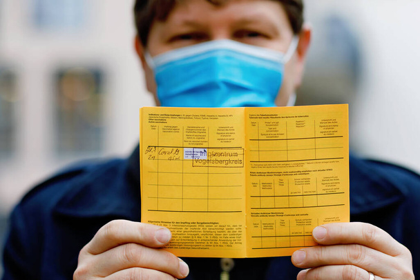 Людина з медичною маскою, що тримає німецький інерційний сертифікат вакцинації. Він показав інформацію про свою вакцину проти вірусу конід 19.. - Фото, зображення