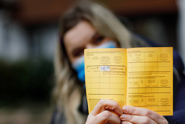 Donna con maschera medica in possesso di certificato internazionale tedesco della vaccinazione. Adulti che mostrano le informazioni sul vaccino contro il virus della covd 19 corona. - Foto, immagini