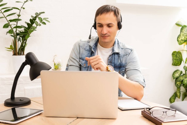 Focused young businessman in eyewear wearing headphones, holding video call with clients on laptop. Concentrated millennial man in glasses giving online educational class lecture, consulting customer. - Photo, Image