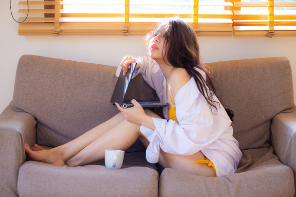 Young asian woman using laptop business connection while sitting on comfortable sofa, home interior - Φωτογραφία, εικόνα