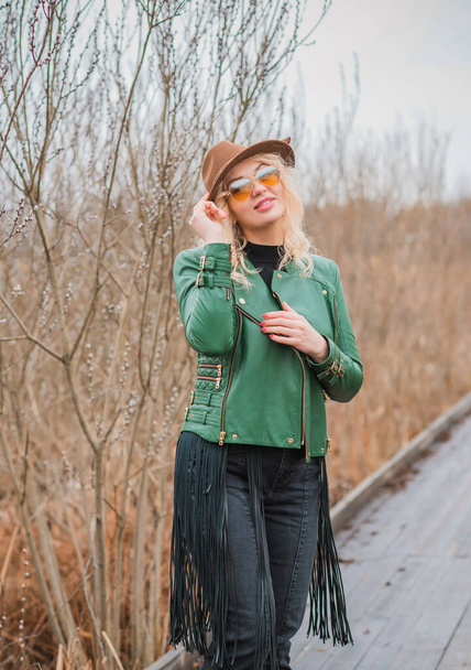 Kadın, eko-deri yeşil ceket, Fedora kahverengi şapka ve eski model havacı gözlükleri giyiyor, püsküllü kemer, moda konsept.  - Fotoğraf, Görsel
