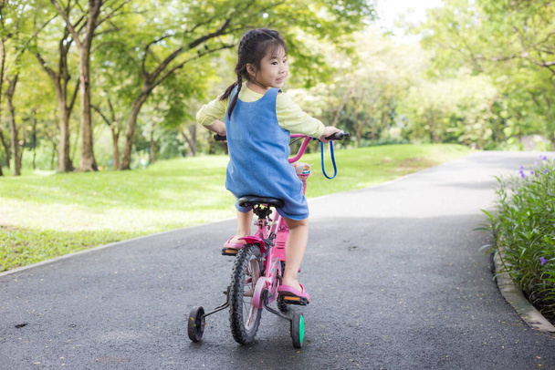 Yaz kenti parkında bisikletli küçük Asyalı kızın portresi. Açık hava çocuğu egzersizi. - Fotoğraf, Görsel