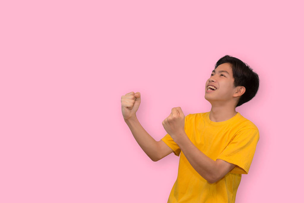 Šťastný vzrušený mladý asijský muž zvedá pěsti dělá ano gesto slaví úspěch v prázdném prostoru stranou v izolovaném studiu růžové pozadí - Fotografie, Obrázek
