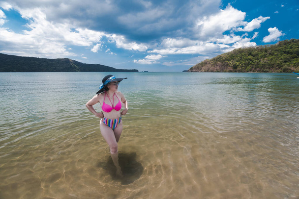 Uma senhora asiática em um biquíni de cintura alta admira a paisagem na praia. Aventura e fim de semana fuga tema. - Foto, Imagem