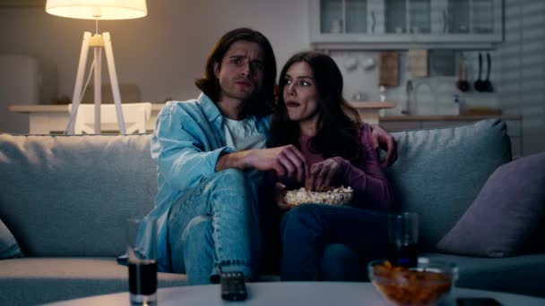 Wewnątrz ujęcie młodej, skoncentrowanej pary zakochanej w miłości oglądającej film z popcornem, spędzającej wieczór w domu, spowolniony ruch - Materiał filmowy, wideo