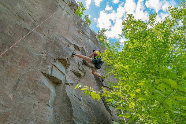 Mujer escaladora con equipo de equipo de escalada sube a la pared de roca. Rocas del cañón en bosque verde - Foto, Imagen